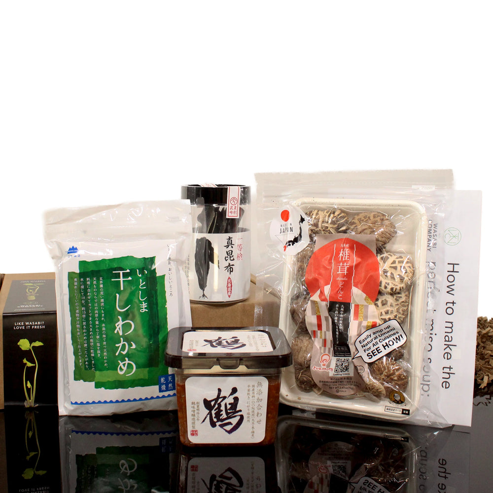 The Vegan Miso Soup Kit, containing kombu seaweed, shiitake mushrooms, miso paste, and seasonings, is attractively arranged on a reflective surface.