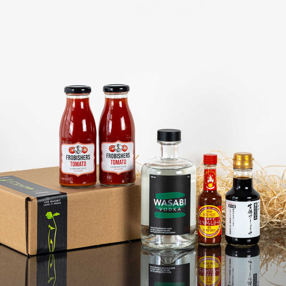 The Wasabi Vodka Bloody Mary Cocktail Kit, featuring Frobishers tomato juice, Wasabi Vodka, Tabasco sauce, and Nama Shoyu Soy Sauce, is arranged on a reflective surface with a brown box and straw in the background.
