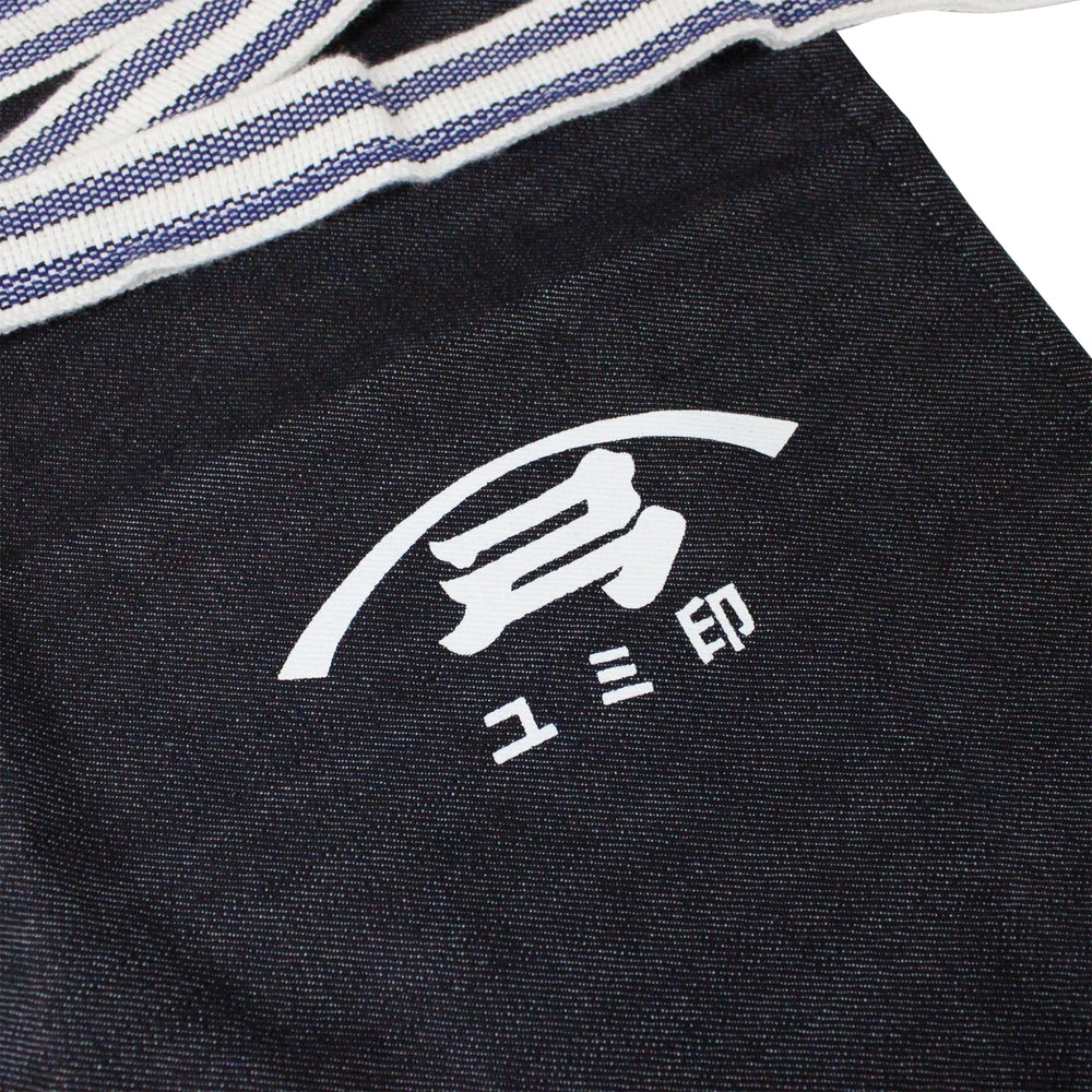 
                  
                    The Yugeta Shoyu Apron is a dark cloth apron with a white logo of Japanese characters and a curved line, partially covered by striped fabric.
                  
                