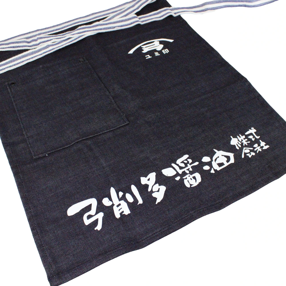 The Yugeta Shoyu Apron is a dark blue denim apron with bold white kanji and logo, a spacious front pocket, and striped waist ties—combining Japanese heritage and practical style.
