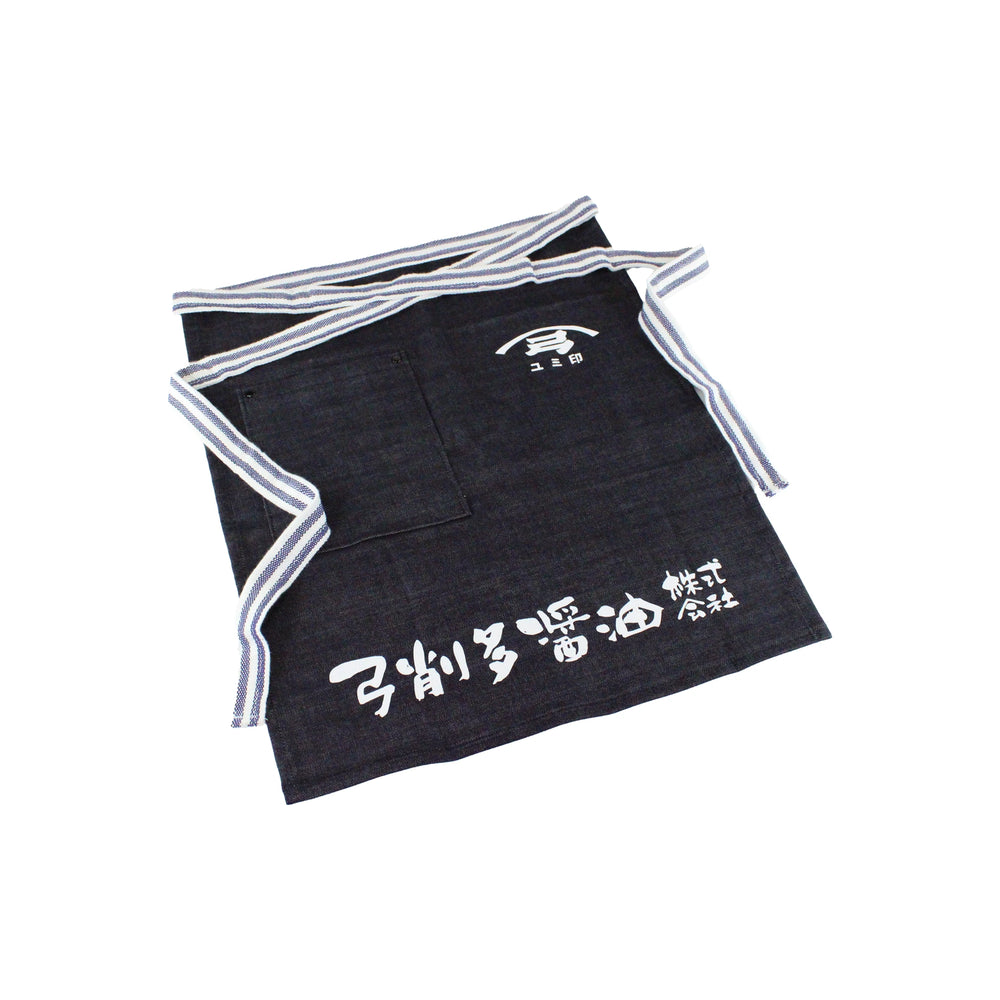 A Yugeta Shoyu Apron in dark blue, featuring white kanji characters and a striped waistband, is displayed flat on a white background.