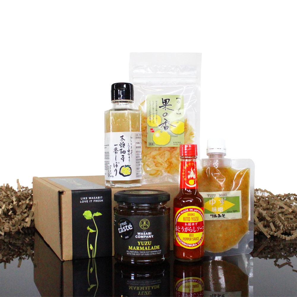 The Yuzu Taster Collection showcases Japanese yuzu flavors with marmalade, sauces, dried lemon slices, and condiments arranged around a brown box.