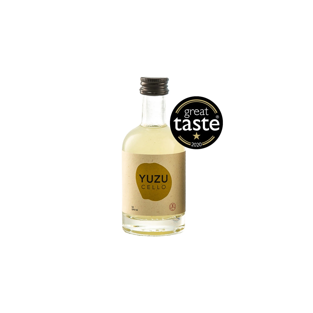A clear glass bottle of Yuzucello - 5cl citrus yuzu liqueur stands beside a black Great Taste 2020 award badge on a white background.