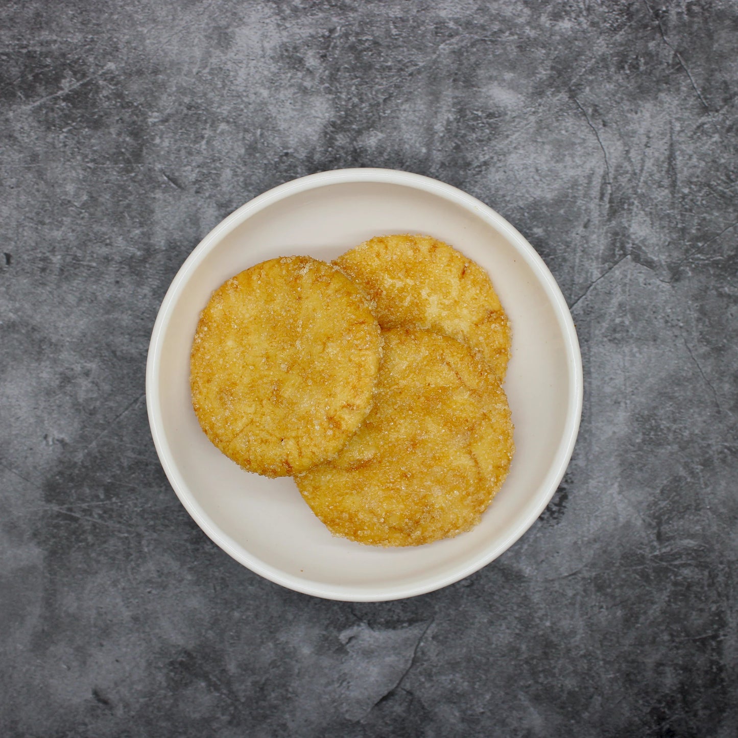 
                  
                    Three round, golden-brown Japanese Rice Crackers - Zarame Senbei 96g rest on a white oval plate atop a textured gray surface.
                  
                