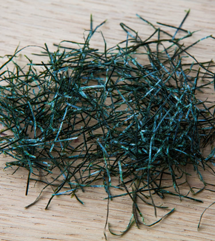 
                  
                    A small pile of Nori Seaweed Angels Hair Cut - 30g rests on a light wooden surface, showcasing the premium product’s thin, delicate texture.
                  
                