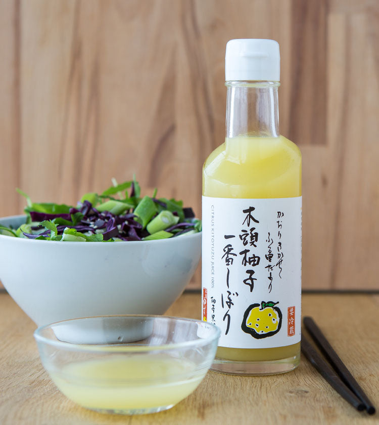 
                  
                    A bottle of Fresh Yuzu Juice from Kito is placed next to a small glass bowl of yuzu juice and a salad with chopsticks on a wooden surface.
                  
                