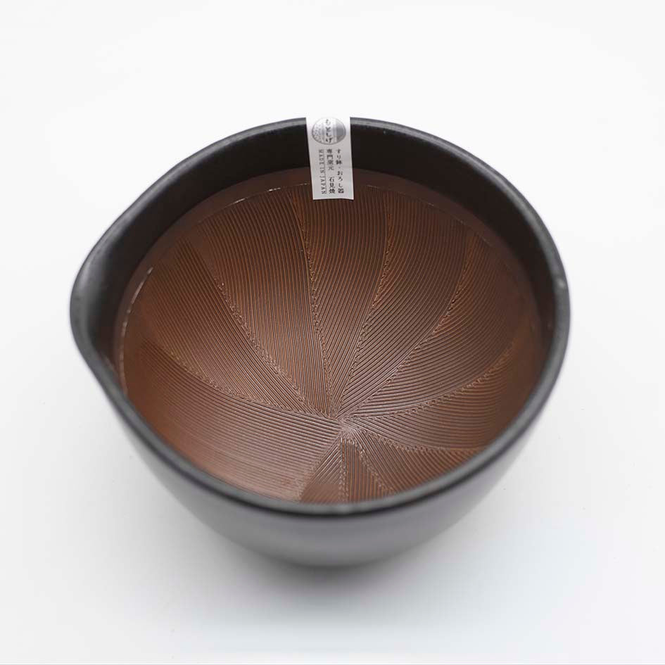 
                  
                    The Suribachi Motoshige Pestle & Mortar - Black features a black ceramic bowl with a brown, ridged interior and small spout, plus a rim label in Japanese—ideal for grinding ingredients in Japanese cuisine.
                  
                