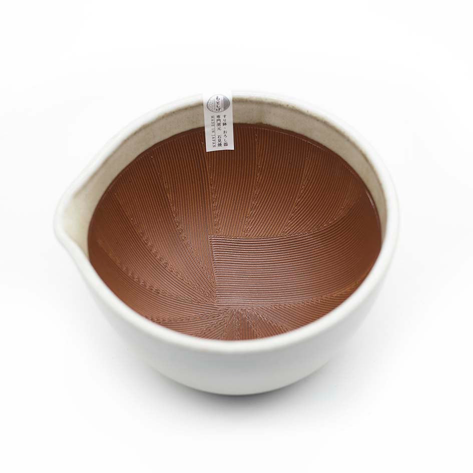 The Suribachi Motoshige Pestle & Mortar - White is a ceramic earthenware mortar with a ridged brown interior, perfect for grinding sesame seeds in Japanese cuisine, and has a small label on the rim.