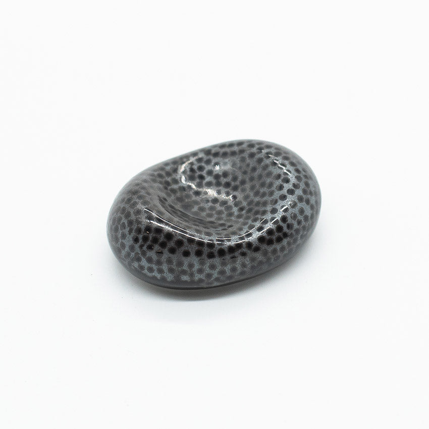 This Chopstick Rest - Pebble Shape Fine Dots features a smooth, oval black porcelain design with fine light gray spots, handmade in Japan for a unique and elegant dining accent.