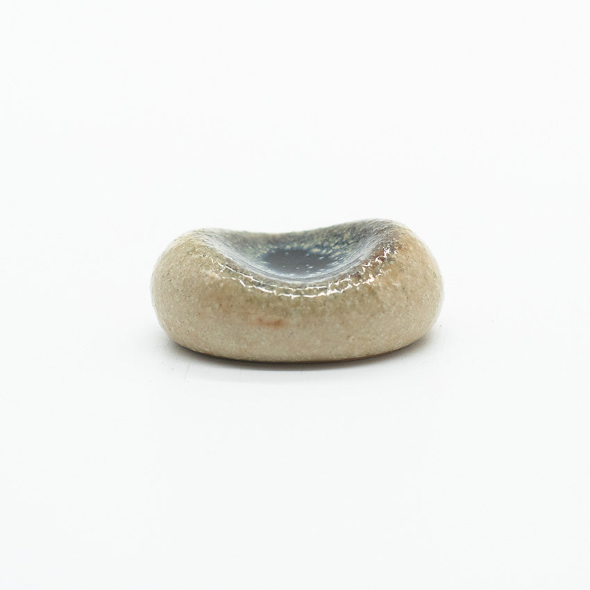 The Chopstick Rest - Pebble Shape Marble is a small, smooth, handmade ceramic accessory with a shallow, darkened center, displayed on a plain white background.