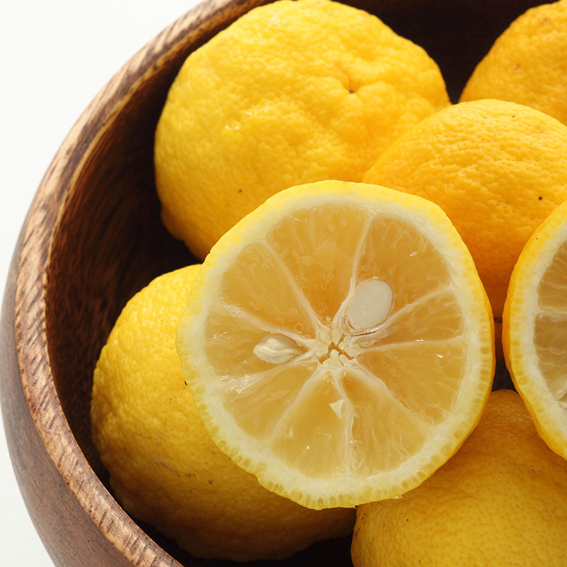 
                  
                    A close-up of several whole Fresh Yuzu and one cut in half, arranged in a wooden bowl, highlights the vibrant appeal of this Japanese citrus fruit.
                  
                