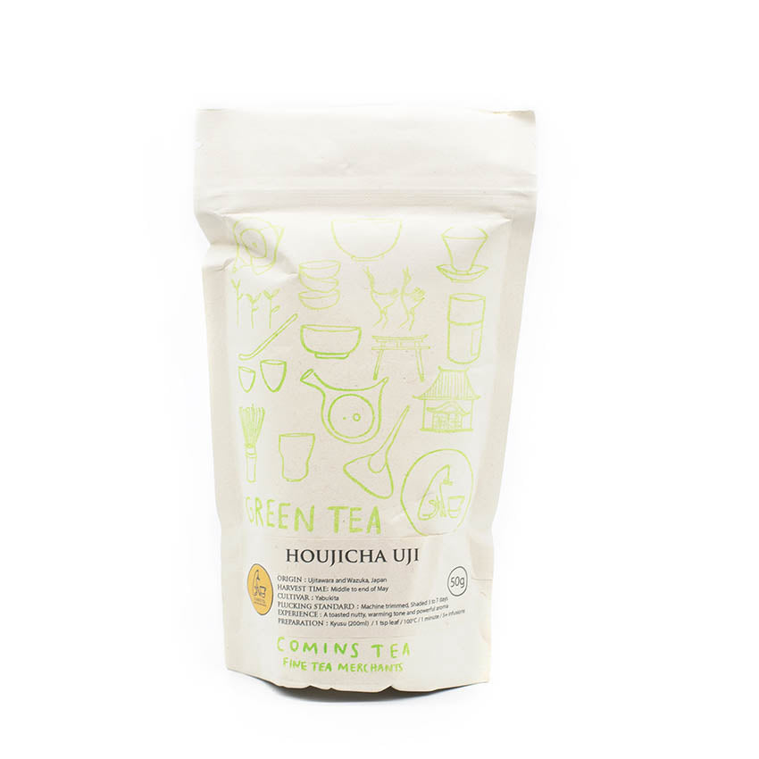 A white resealable pouch labeled Houjicha Tea - 50g from Comins Tea, with light green tea-themed illustrations. This pan roasted blend offers a nutty flavor and less caffeine.