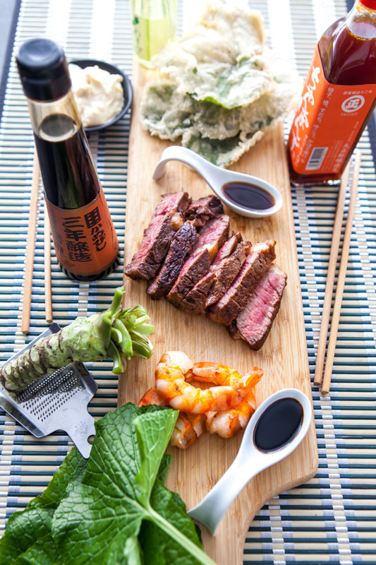
                  
                    Sliced steak, shrimp, tempura vegetables, sushi, Small Fresh English Wasabi Rhizomes 200g, sauces, and condiments are arranged on a wooden board with chopsticks atop a striped placemat.
                  
                