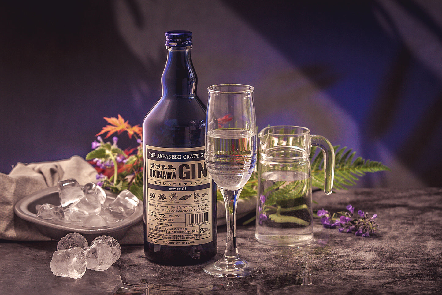 
                  
                    A bottle of Okinawa Gin - 700ml, a gin-filled glass, a herb pitcher, ice cubes, and flowers—showcasing distinct Okinawan botanicals—are stylishly arranged on marble.
                  
                