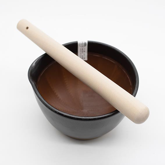 
                  
                    The Suribachi Motoshige Pestle & Mortar - Black features a ceramic earthenware bowl with a textured interior and a light wooden pestle, ideal for preparing Japanese cuisine.
                  
                