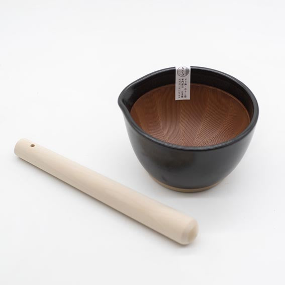 The Suribachi Motoshige Pestle & Mortar - Black features a black and brown earthenware mortar with a textured interior and a light wooden pestle, ideal for preparing Japanese cuisine.