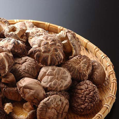 A woven basket filled with Wasabi Label Organic Dried Donko Shiitake Mushrooms (70g) is set against a dark background.