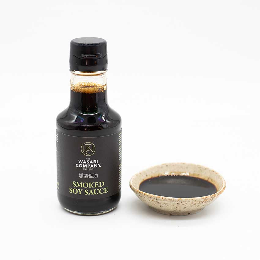 
                  
                    A Soy Sauce Dish - Sand Fade sits beside a bottle of Wasabi Company smoked soy sauce, both set against a white background. Made in Japan.
                  
                