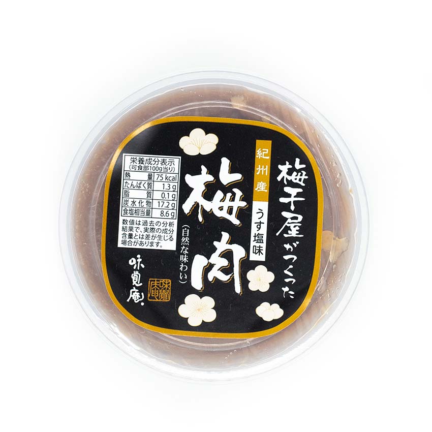 A round plastic container labeled with Japanese text and plum blossom motifs holds 100g of Umeboshi Paste. The lid displays nutritional information.