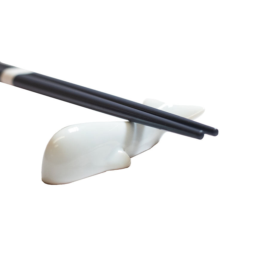 Black chopsticks rest on the Whale Chopstick Rest - White, crafted from Minoyaki porcelain in a whale shape, set against a plain white background.